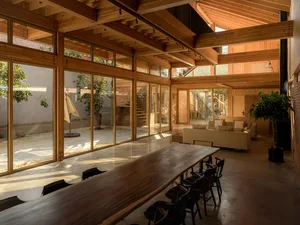 Modern minimalist living room with wood accents and furniture, featuring a long wooden table, black chairs, and a cozy seatin