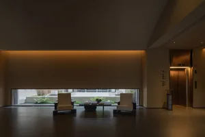 A minimalist lobby with glass walls, featuring a sleek table and two chairs.
