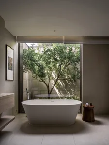 Modern minimalist bathroom featuring a freestanding bathtub with concrete walls and a large window overlooking a tree.