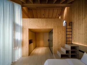 A minimalist bedroom featuring wooden walls and a white bed, with a ladder leading up to an upper floor.