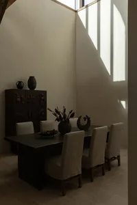 A minimalist dining room with a wooden table and chairs, featuring a vase of flowers and decorative items