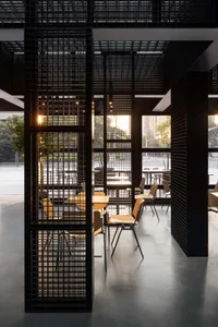 Industrial-style restaurant interior with black lattice walls, concrete flooring, and chairs with wooden seats.