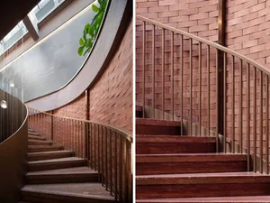 A modern, curved staircase with wooden steps, metal handrails, and brick walls.