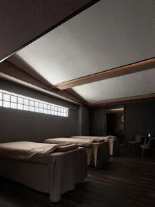 Spa room with three massage beds covered with brown fabric, dark interior, and small window with square glass panels.