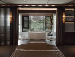 A minimalist spa room with a circular stone tub, wooden floor, and glass walls.