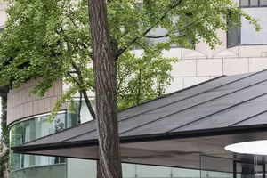 A modern building with a metal roof and surrounding greenery.
