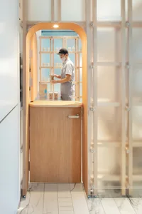 A person wearing a black cap and face mask stands behind a wooden coffee bar.