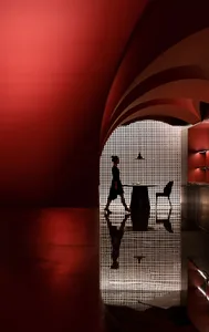 A modern space with red walls and a black grid pattern on the floor and ceiling, featuring a woman walking through the archwa