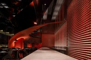 A modern restaurant interior with a red metallic tile wall and sleek bar counter.