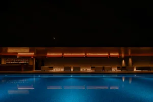 Modern studio with glass walls and a swimming pool at night.