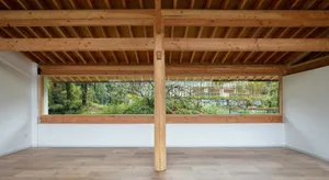 Minimalist living room featuring a wooden floor and ceiling, with a large window overlooking greenery.