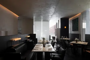 A modern restaurant with concrete walls and benches, featuring sleek furniture and minimalist decor.