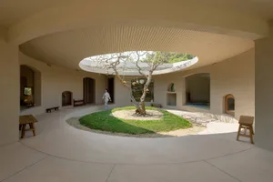 A modern living space featuring a circular, concrete patio with a central tree, benches, and arches.