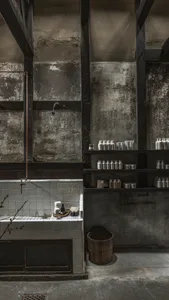 A modern, industrial-style bathroom with concrete walls and exposed beams, featuring a shower head mounted on the wall and va