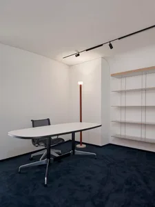 A minimalist office featuring a white-painted wall, dark carpet floors, recessed lighting, and minimalist shelving.