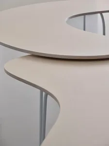 A modern furniture table with a curved, wooden tabletop and white metal legs.