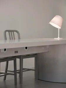 A minimalist office desk setup featuring a white desk, two stools, and a modern table lamp.