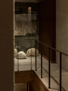 A staircase with a glass railing overlooking ceramic sculptures and a landscaped area with trees and plants.