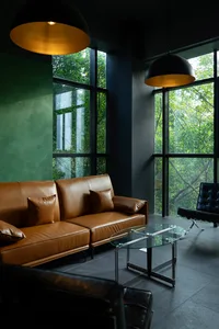 A modern living room featuring a brown leather sofa with glass coffee table and concrete walls.