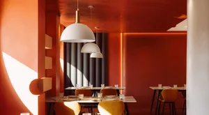 A modern restaurant interior featuring white pendant lights hanging from an orange ceiling.