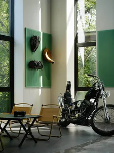 A living room with a black motorcycle parked indoors, featuring wooden chairs and a metal table with a black camera on it.