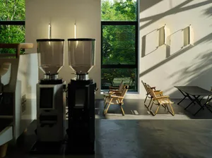 A minimalist cafe interior featuring wooden furniture and large windows with views of greenery.