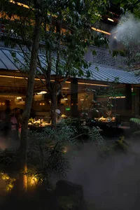 Outdoor view of an industrial-themed restaurant with metallic accents, glass walls, and a concrete structure.