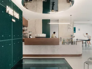 A modern cafe interior with a concrete and tile counter, featuring a coffee machine and a man working behind it.