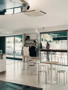 A modern coffee shop with minimalist design featuring a concrete floor, white stools, and tables.