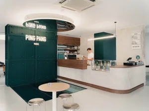 A modern minimalist cafe interior featuring white walls, wooden counter, and green tiles with white lettering.