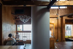 A modern restaurant interior with wooden walls and seating areas, featuring a chandelier and a glass partition.