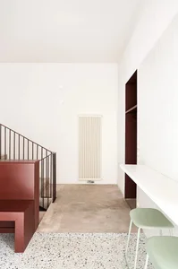 A minimalist interior with a concrete floor, white walls, and a simple red staircase.