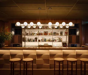 Industrial-style bar with wooden stools, featuring an extensive backlit liquor collection and ambient lighting.