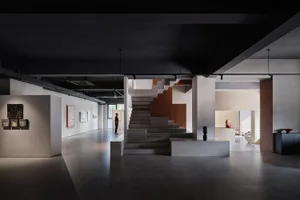 A modern art gallery space featuring minimalist design, concrete walls, and metal accents.