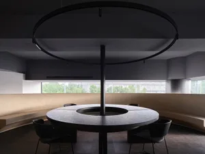 A modern conference room with a circular table made of concrete, surrounded by black chairs, and featuring a circular lightin