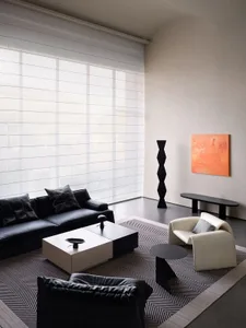 Modern living room featuring a black leather sofa, white and black side tables, and an abstract orange painting on the wall.