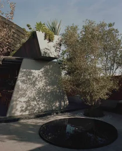 A modern concrete landscape design featuring a circular water feature, greenery, and geometric planters.