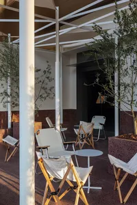 Outdoor seating area with modern, foldable chairs and small white tables under a large canopy, surrounded by greenery.