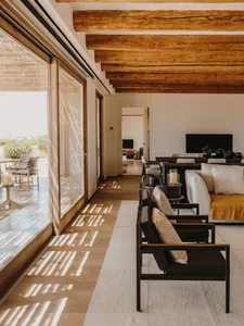A modern, minimalist residential living room with indoor-outdoor design elements, featuring wood, glass, and metal materials.