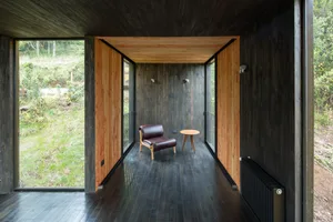 A minimalist room with wooden floors, walls, and panels, featuring a brown leather chair and small wooden table.