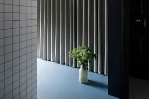 A minimalist interior featuring a gray curtain, vase with greenery, and minimalist decor.