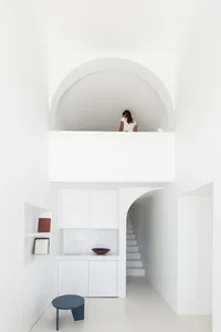 A minimalist white residential interior with concrete accents and a blue stool.