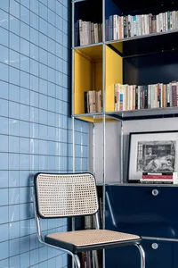 A modern interior featuring a metallic shelving unit with blue tiled walls, displaying a variety of books and a framed pictur