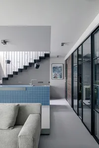 A modern living room featuring blue tiles, concrete flooring, and a large window with glass doors, with a minimalist design.