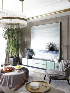 A modern living room featuring a gold chandelier, potted plants, and a painting of a horse's head on a cabinet.