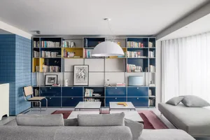 A modern living room with minimalist furniture, a metal and glass bookshelf, and fabric seating.