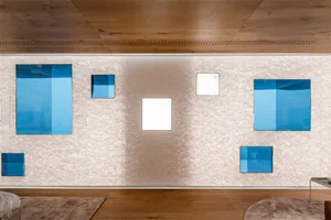 A minimalist installation featuring blue and white paper panels on a textured beige wall, with a brown wooden floor and a whi