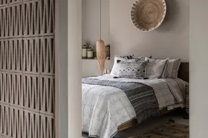 A minimalist bedroom featuring a bed with white and gray textiles made of cotton, a woven basket hanging on the wall, and a t