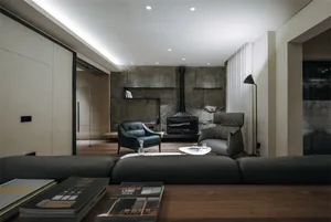 A modern living room with concrete walls, black leather armchairs, and wood flooring.