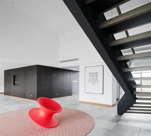 Modern living space with a black steel staircase and a red spiral chair on a round rug.